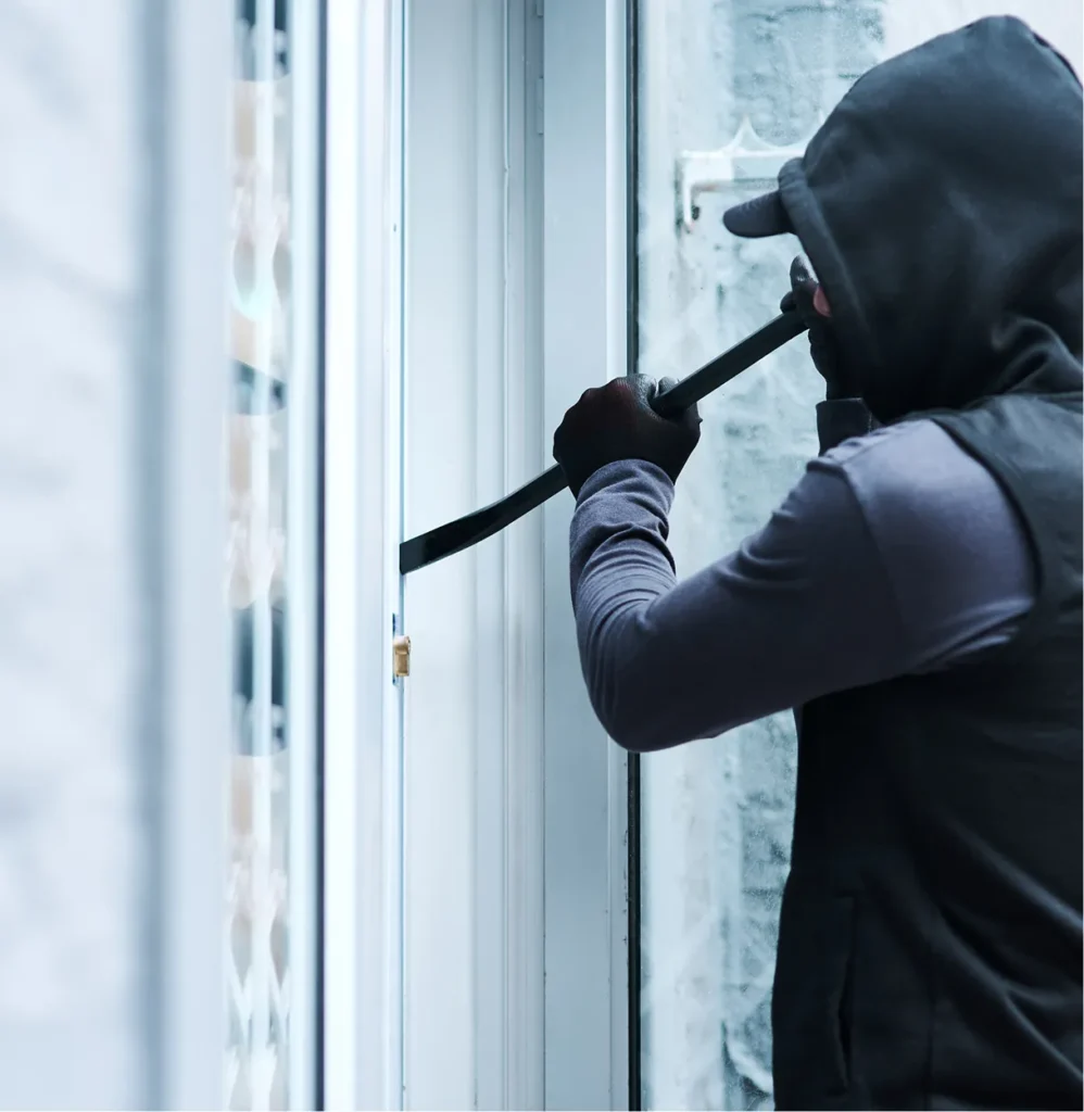 Hooded burglar prying open a window with a crowbar, illustrating scenario-based physical risk modeling for burglary