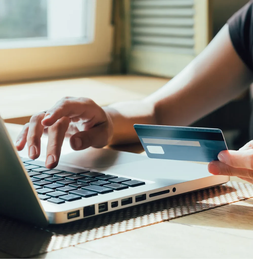 Hands holding a credit card while typing on a laptop, illustrating PCI compliance in physical security