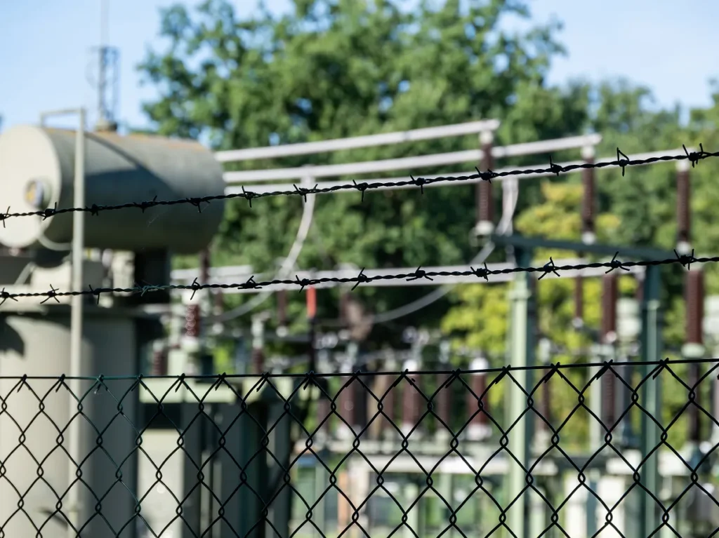Barbed wire and chain-link fence around a utility substation, illustrating critical infrastructure physical security for water and utilities