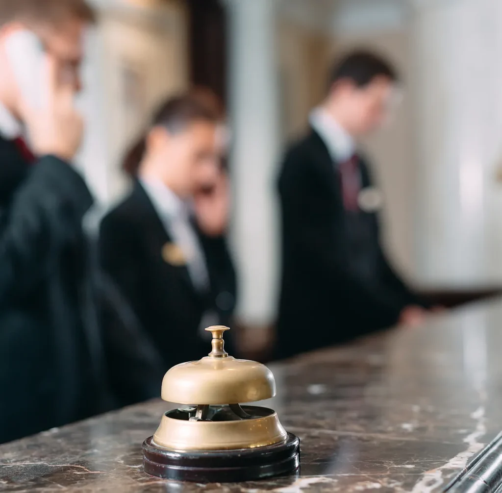Hotel front desk staff on the phone behind a service bell, illustrating physical security risk in hospitality and commercial properties