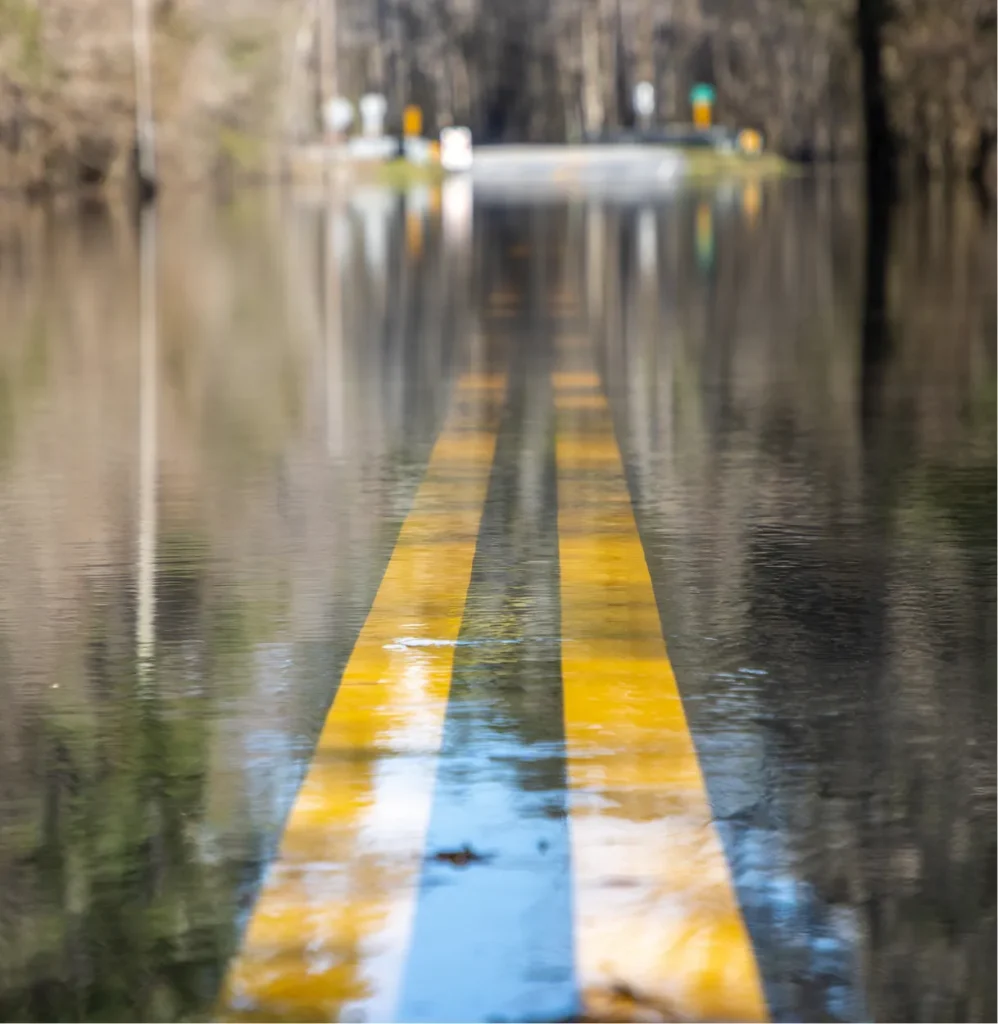 Flooded road with yellow center lines disappearing under floodwater, illustrating hazard scenarios in physical risk modeling