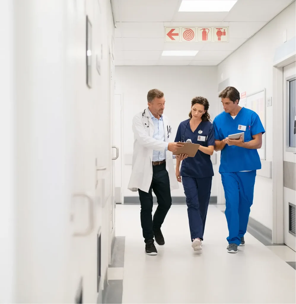 Doctor and two nurses reviewing a chart in a hospital hallway, illustrating compliance frameworks such as Joint Commission standards
