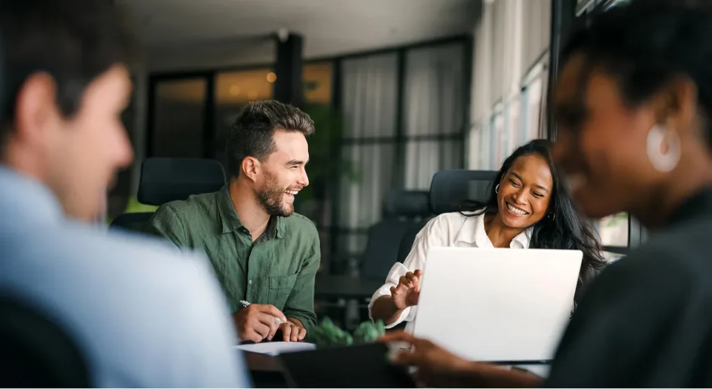 Colleagues laughing together around a laptop in a meeting, for joining the Circadian Risk team