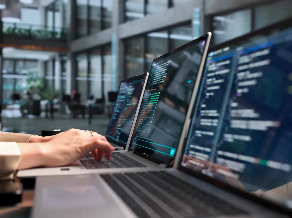 Hands typing on a row of laptops showing code and data, illustrating how ASIS standards fit the compliance picture