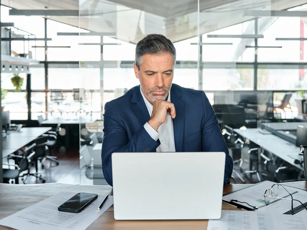 Executive in a blue suit resting his chin on his hand at a laptop, illustrating security capital planning decisions on finite budgets