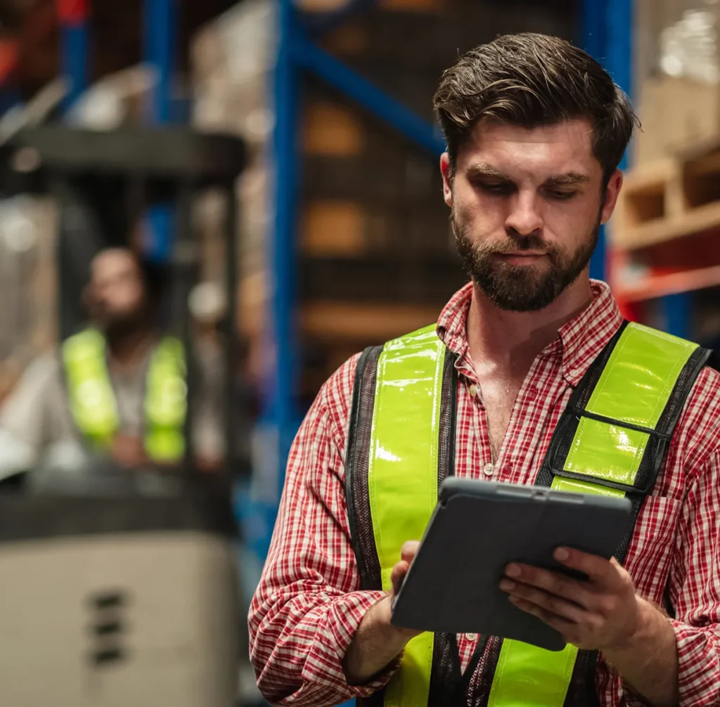 Warehouse worker in a high-visibility vest checking a tablet, illustrating site-level visibility for CSOs, executives and facilities teams