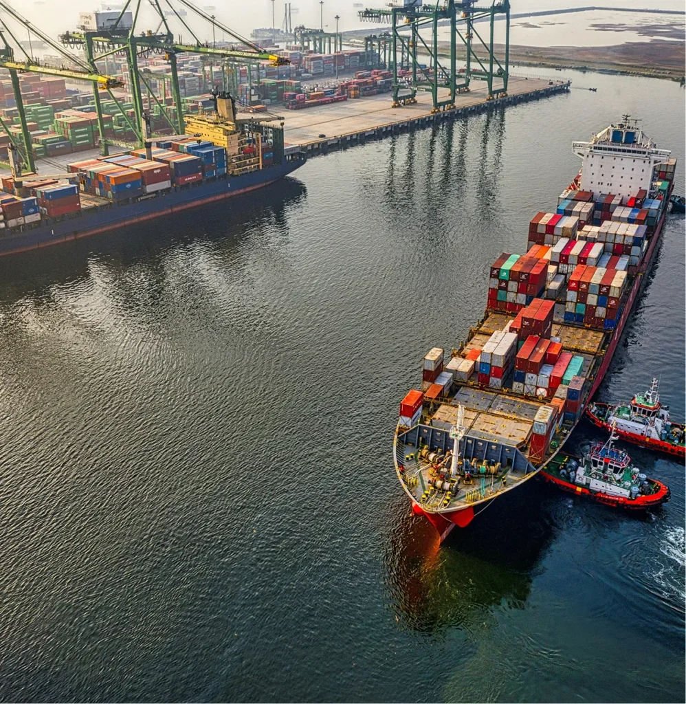 Aerial view of a container ship entering a port with cranes, illustrating supply chain compliance frameworks such as C-TPAT